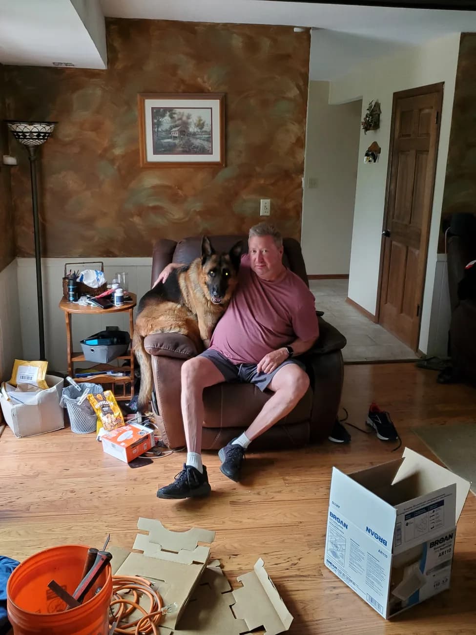 Michael seated in the recliner, the German Shepherd approaching from behind