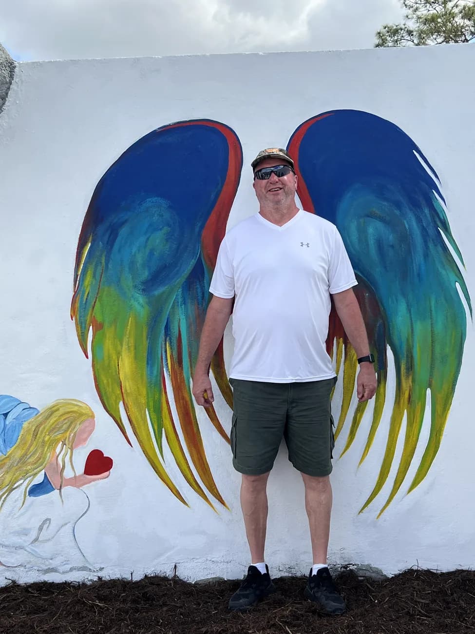 Michael standing in front of a large painted mural of angel wings